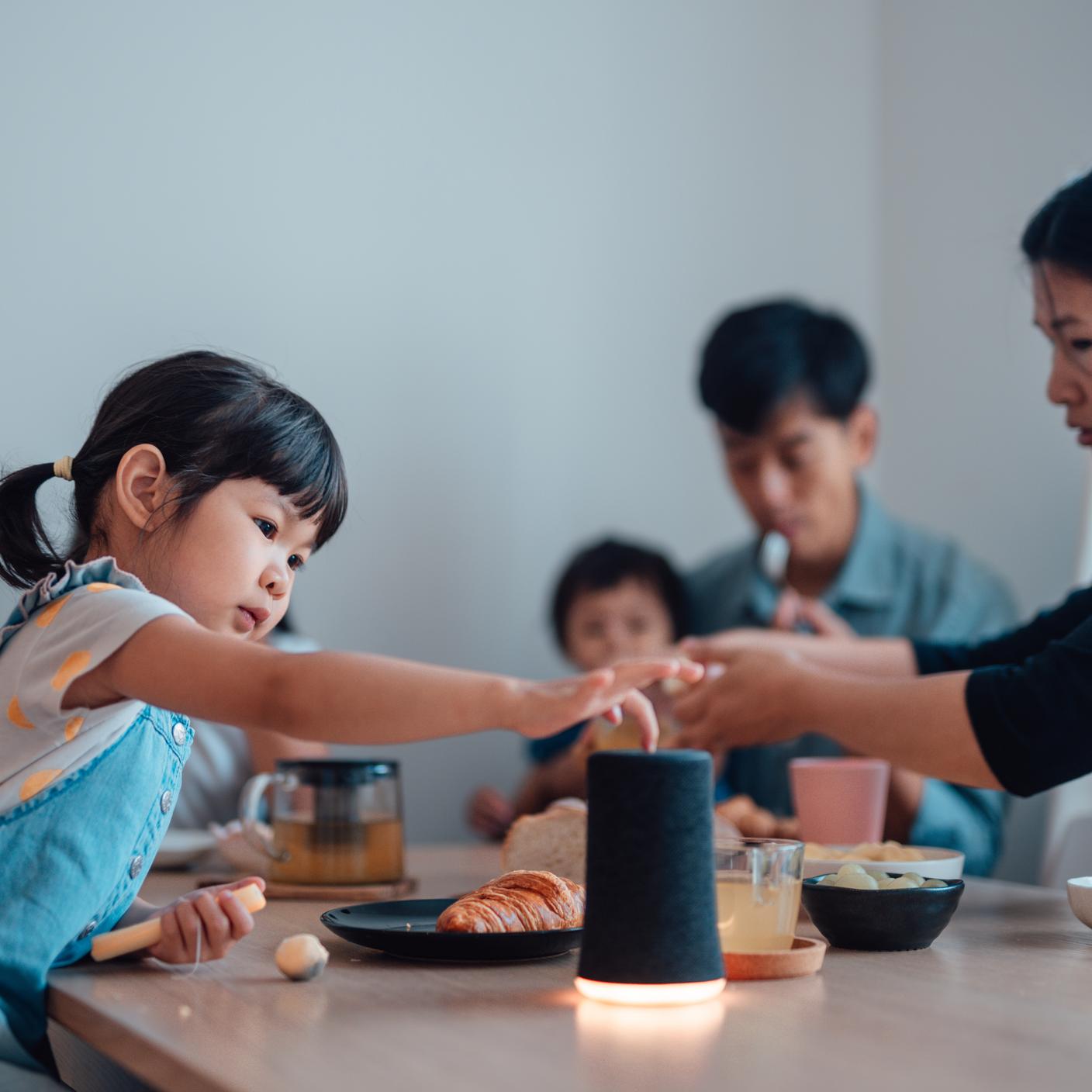 年轻女孩在餐桌边吃早餐时使用智能音箱播放音乐