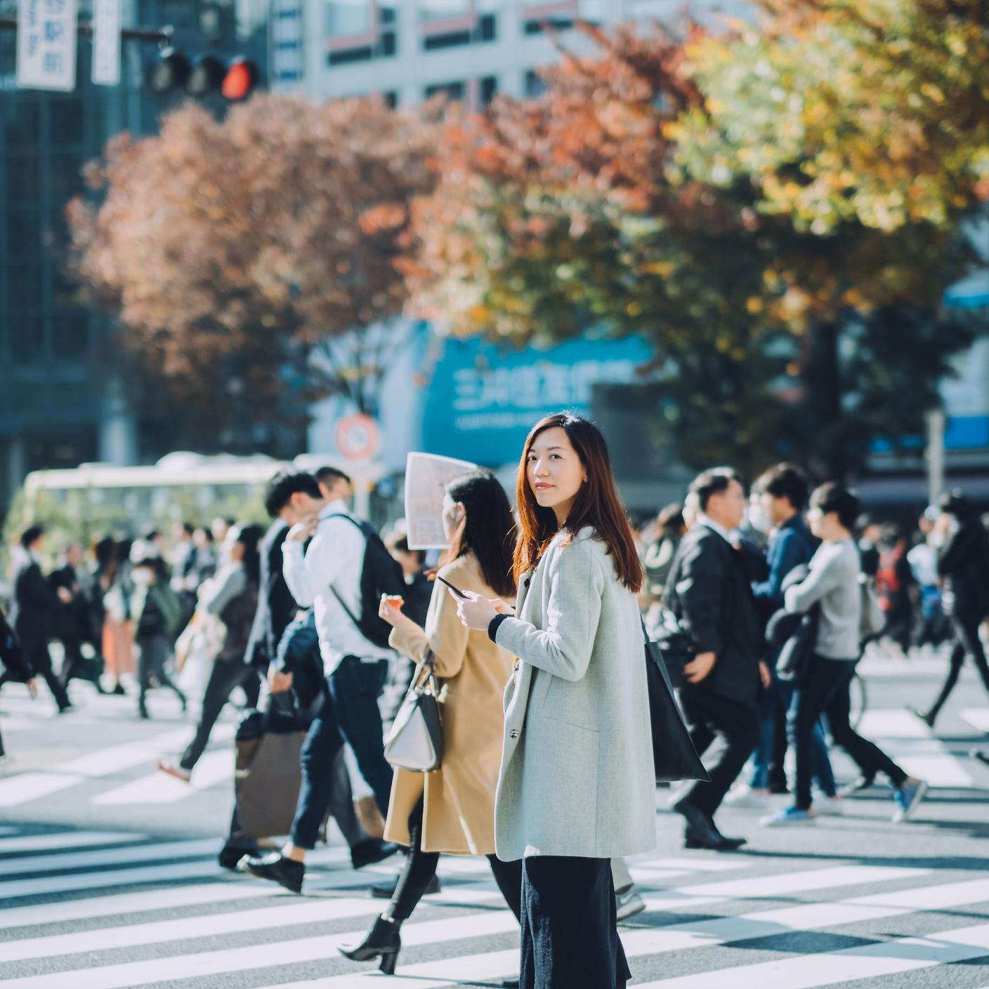 美丽的亚洲女企业家在东京繁忙的街道上边走边使用智能手机